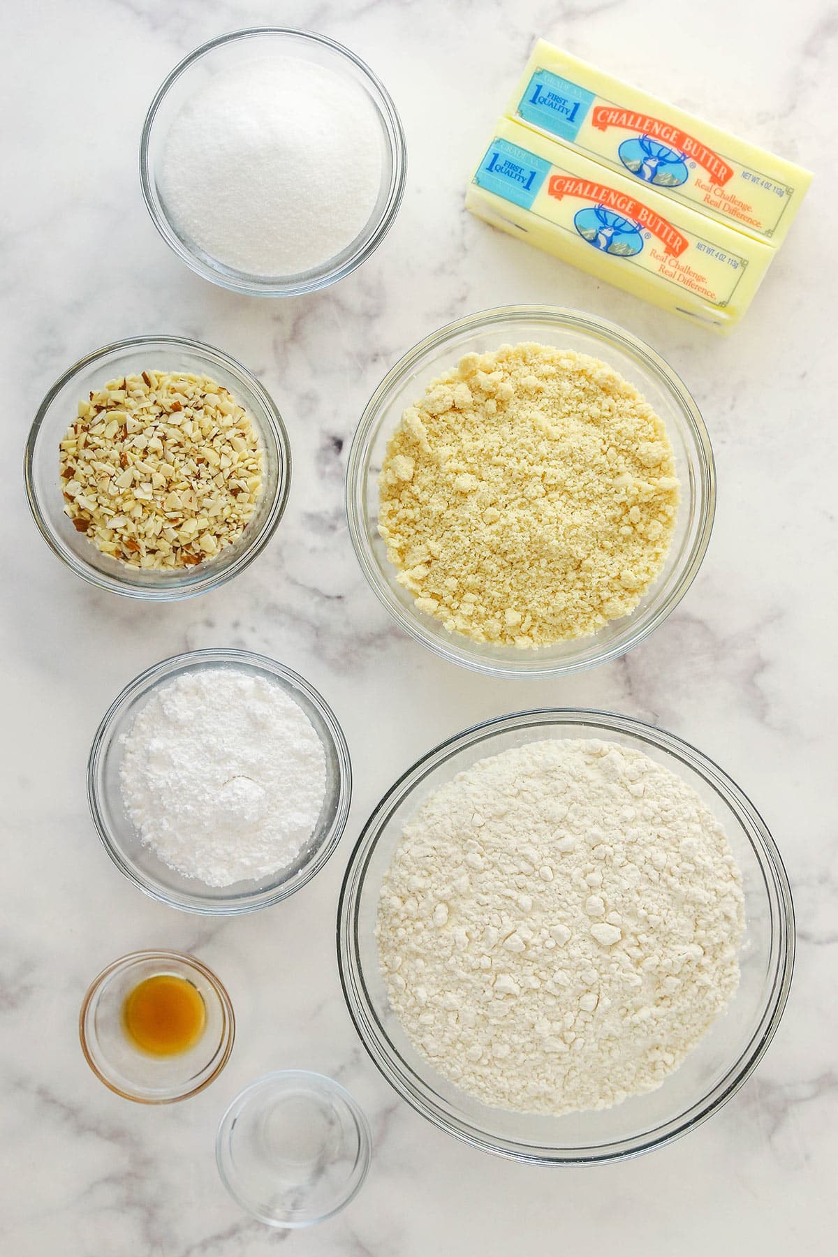 ingredients used in almond crescent cookies in glass bowls on marble background