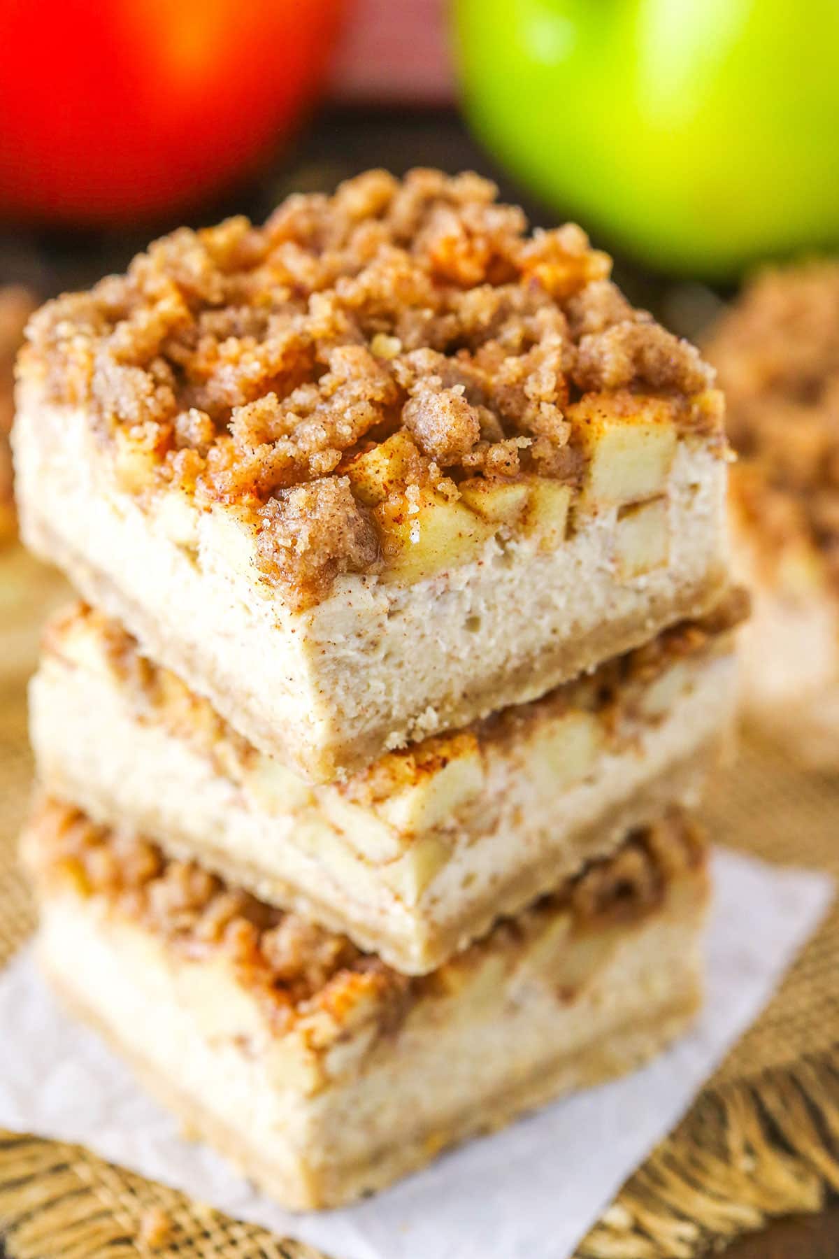 Three Apple Streusel Cheesecake Bars stacked with apples in the background