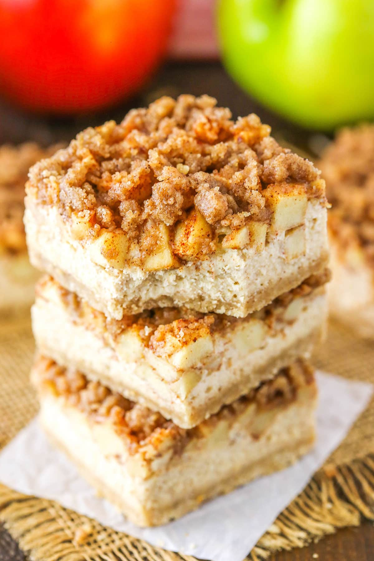 An Apple Streusel Cheesecake Bar with a bite removed stacked on top of two more Apple Streusel Cheesecake Bars
