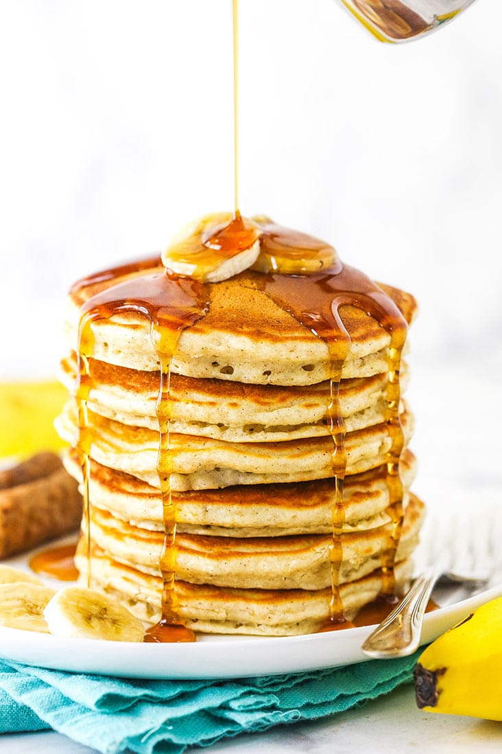 A stack of fluffy banana pancakes with syrup being poured over the top