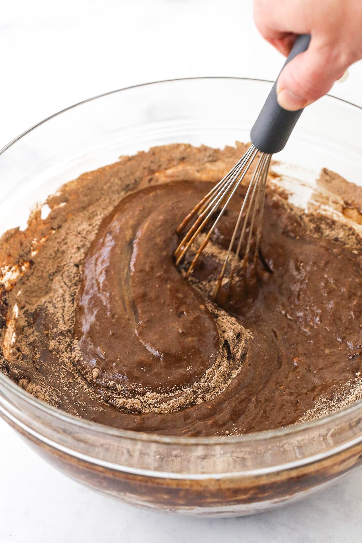 A whisk mixing chocolate cake batter in a glass bowl