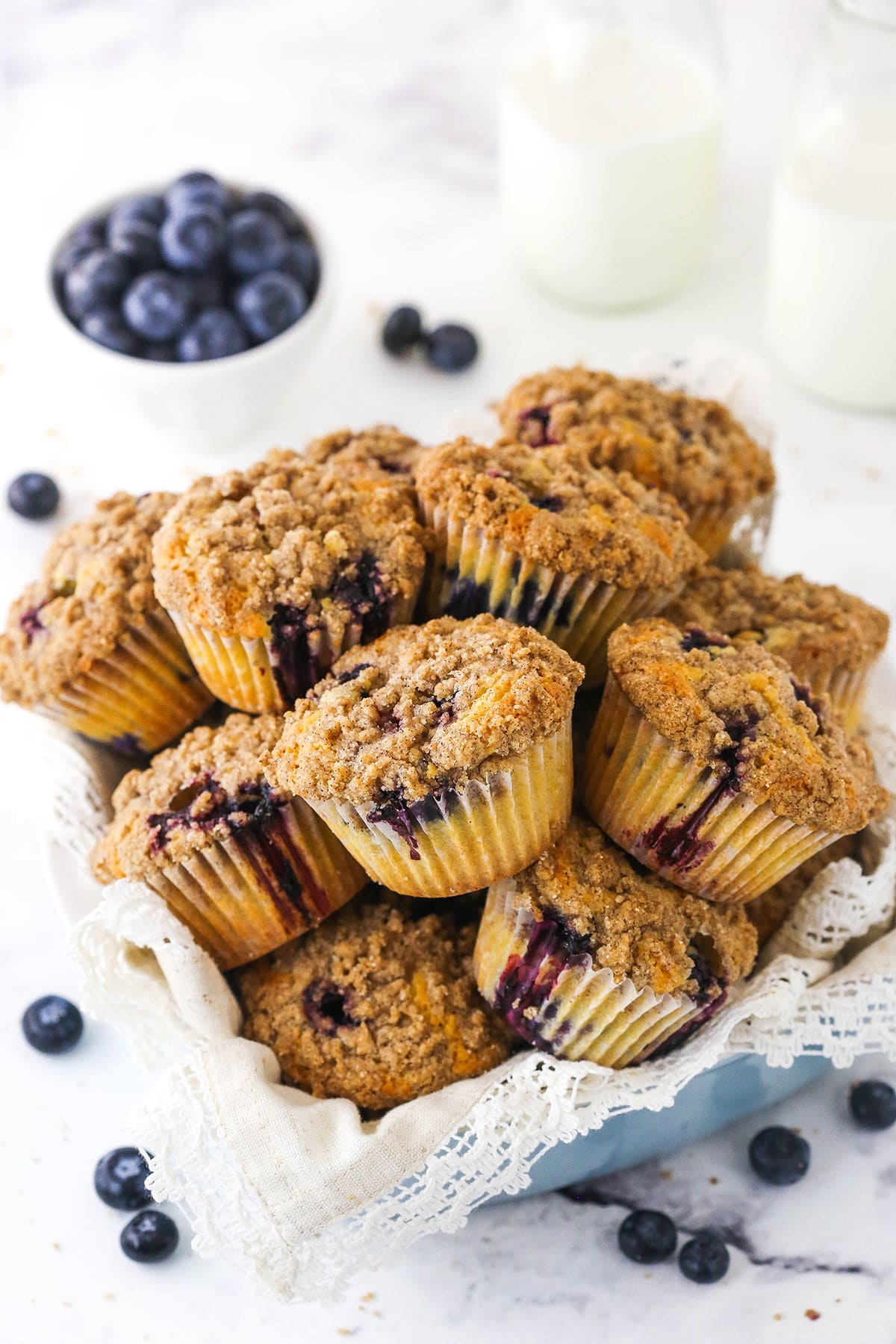 A dish full of blueberry muffins with a bowl of fresh blueberries in the background