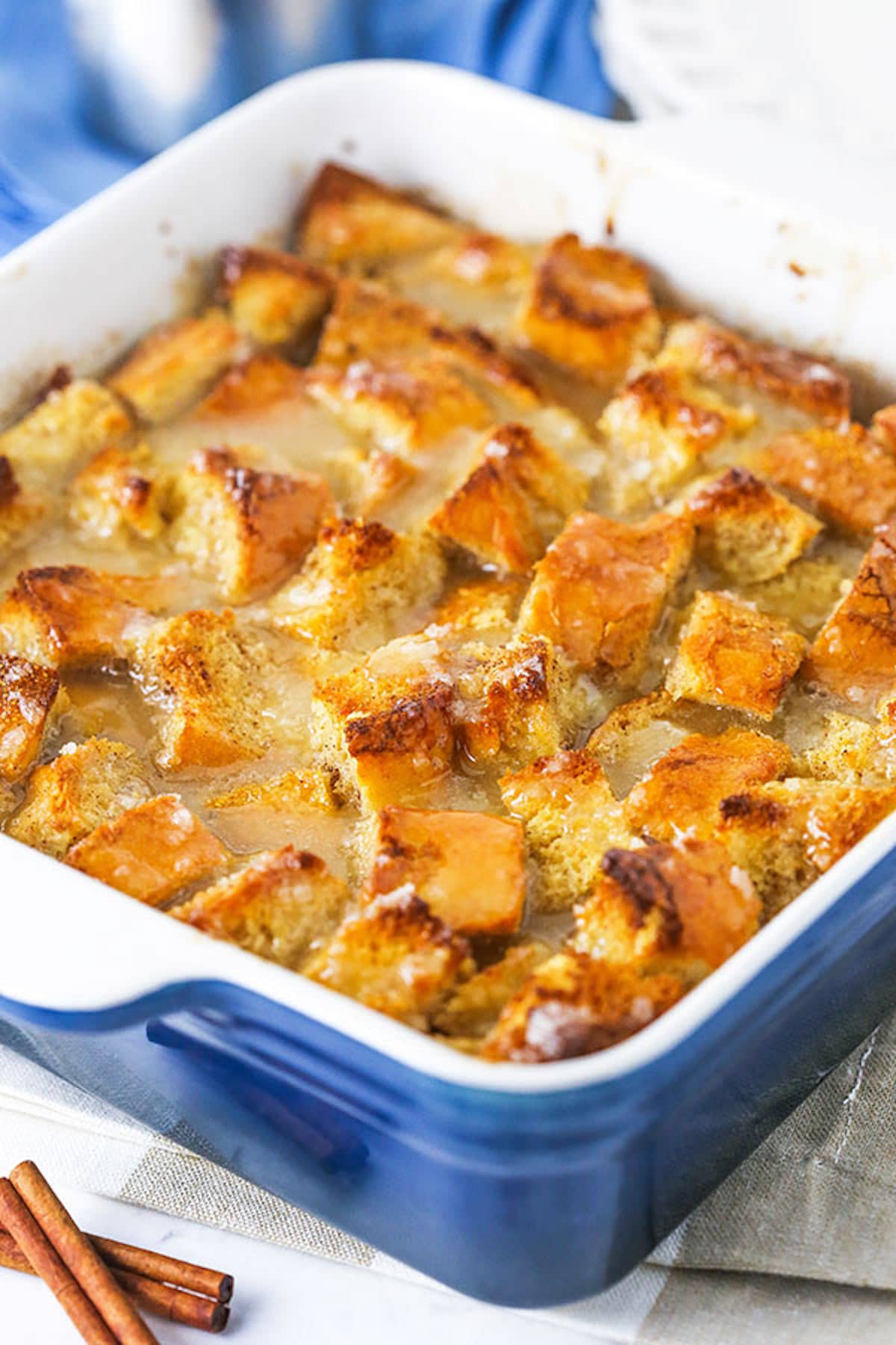 Freshly baked bread pudding in a pan next to two cinnamon sticks.