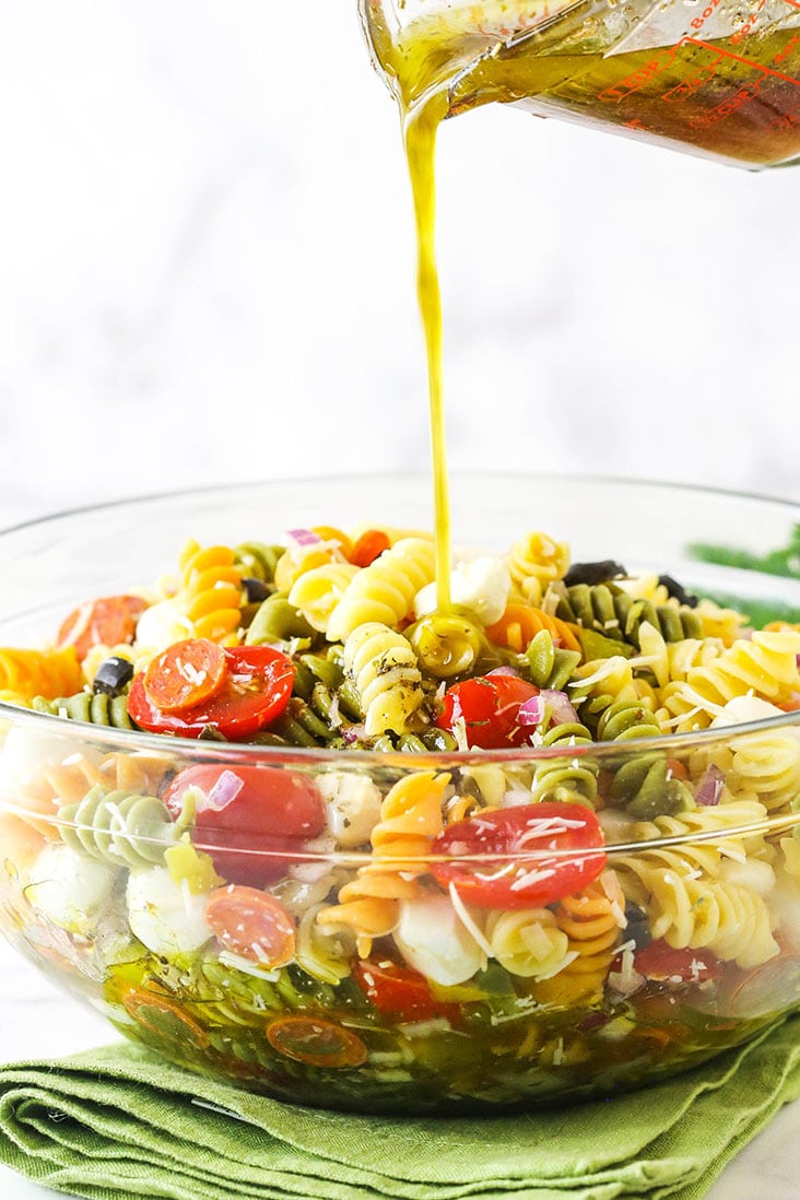 Italian dressing being poured over pasta with vegetables in a glass dish