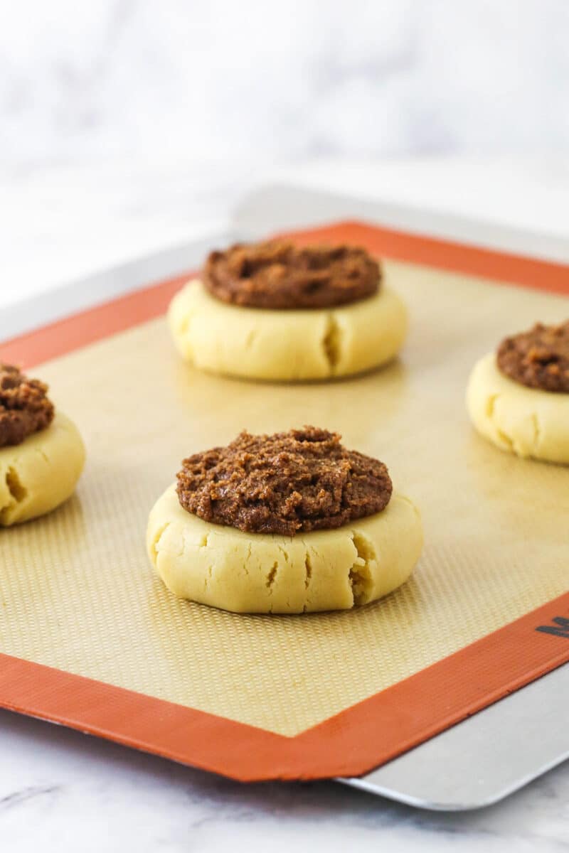 Discs of sugar cookie dough topped with cinnamon filling on a cookie sheet