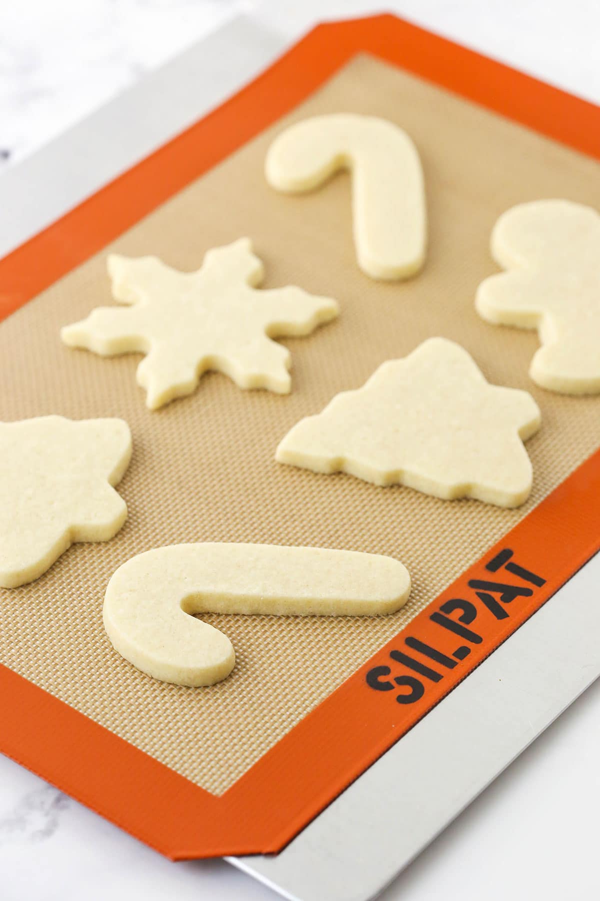 Six baked cut-out sugar cookies on a cookie sheet on top of a marble counter
