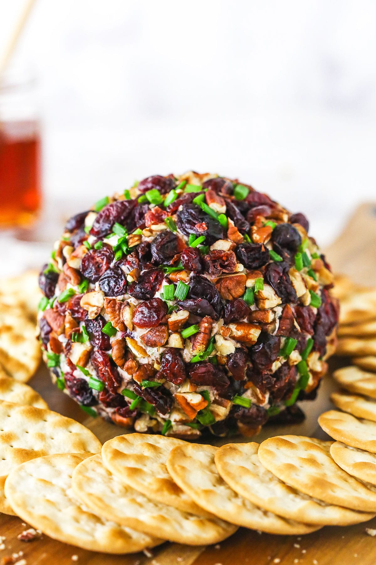 A close-up shot of a cranberry pecan cheeseball on a wooden surface with a white background