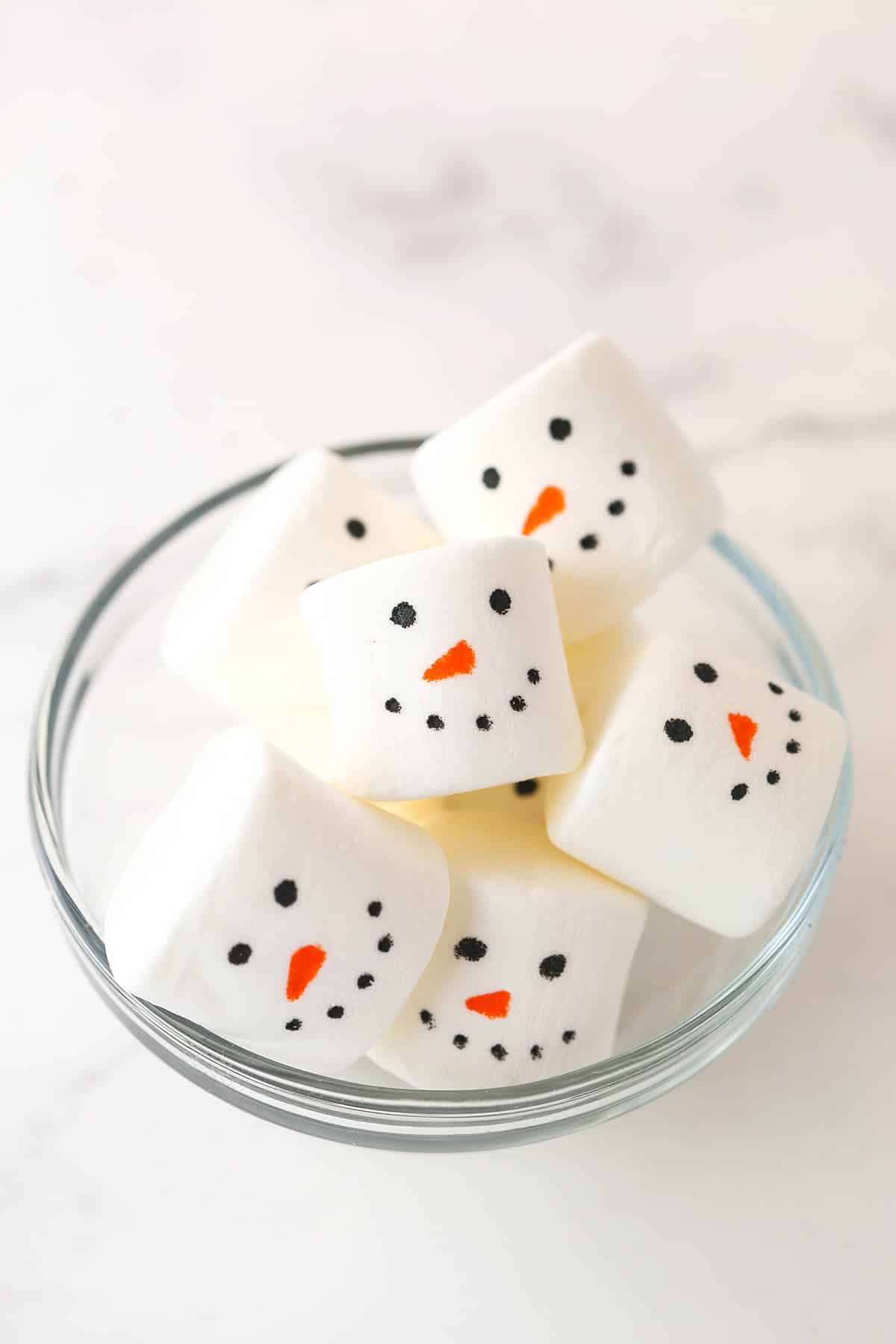 marshmallows with snowman faces drawn on them in a glass bowl