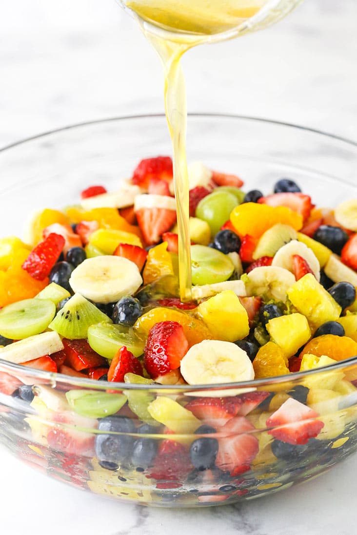 chopped fruit in a clear bowl with dressing being poured on it