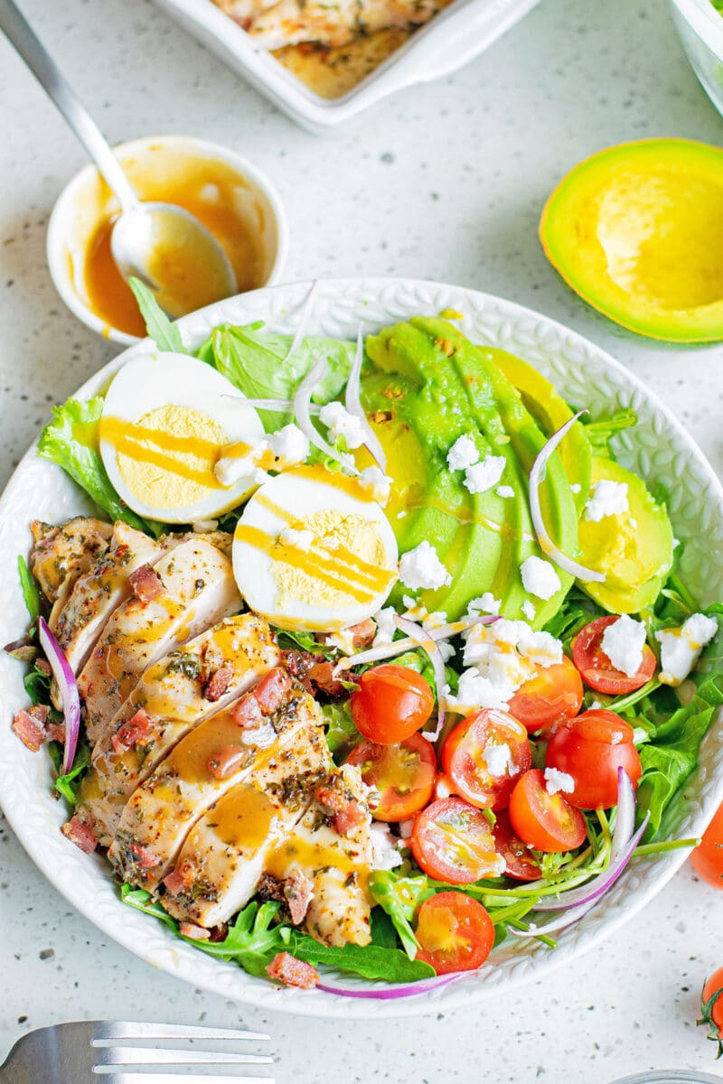 herb chicken cobb salad with dressing in white bowl with dishes around it