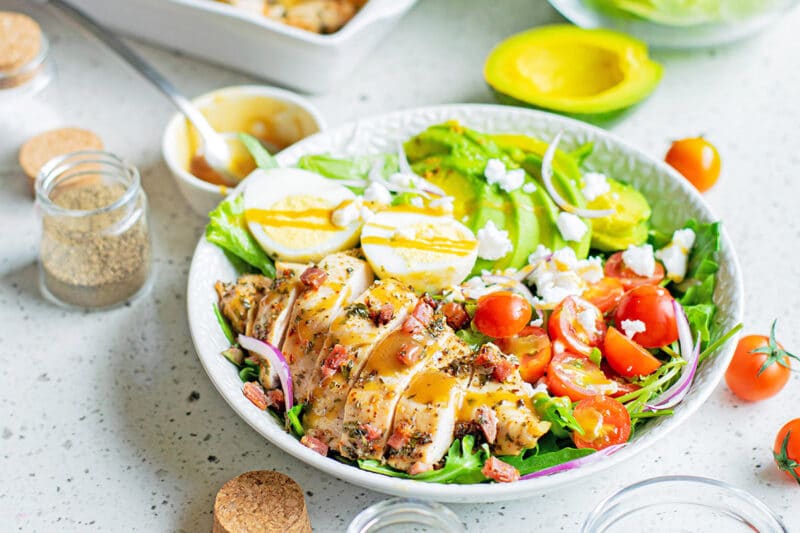 cobb salad on white surface with dishes and ingredients around it