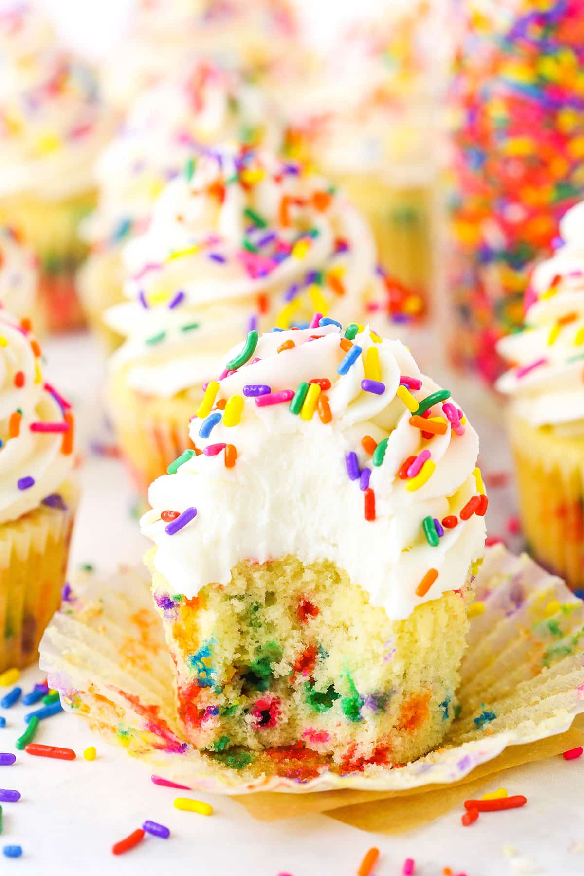 A Homemade Funfetti Cupcake with a bite taken out topped with white frosting and colorful sprinkles
