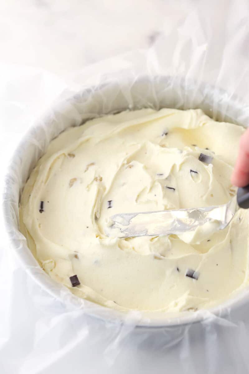 Spreading softened ice cream into a cake pan lined with clear wrap.