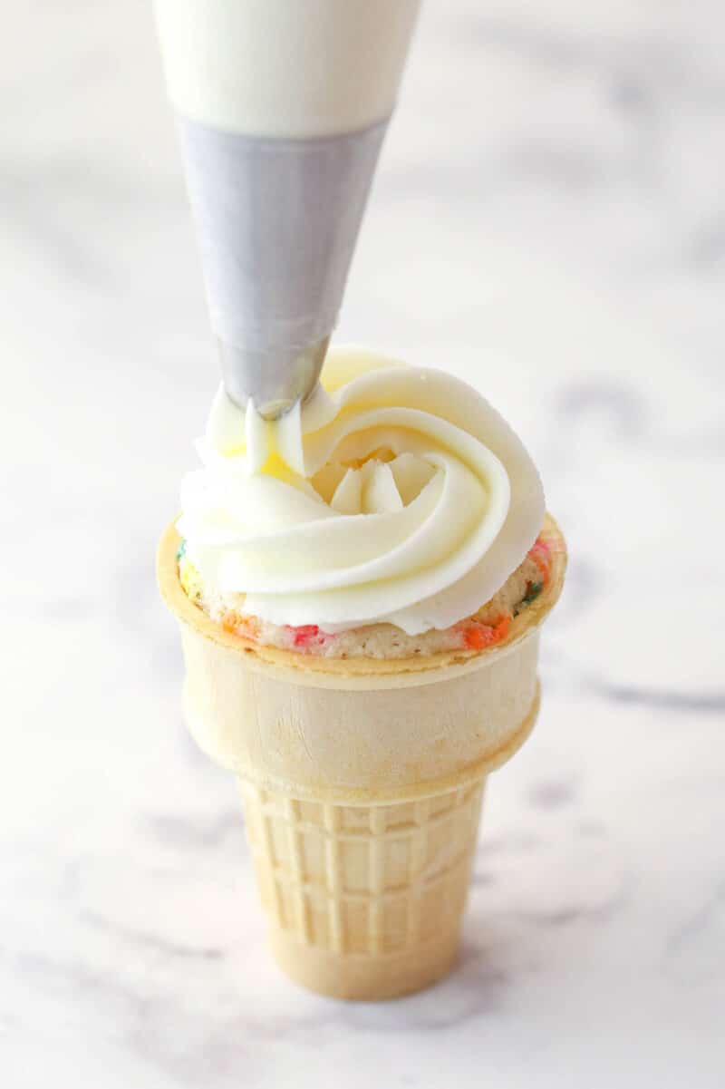 Piping buttercream frosting onto an ice cream cone cupcake.