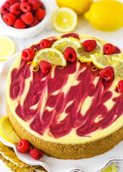 A slice of lemon raspberry swirl cheesecake topped with raspberries and lemon
