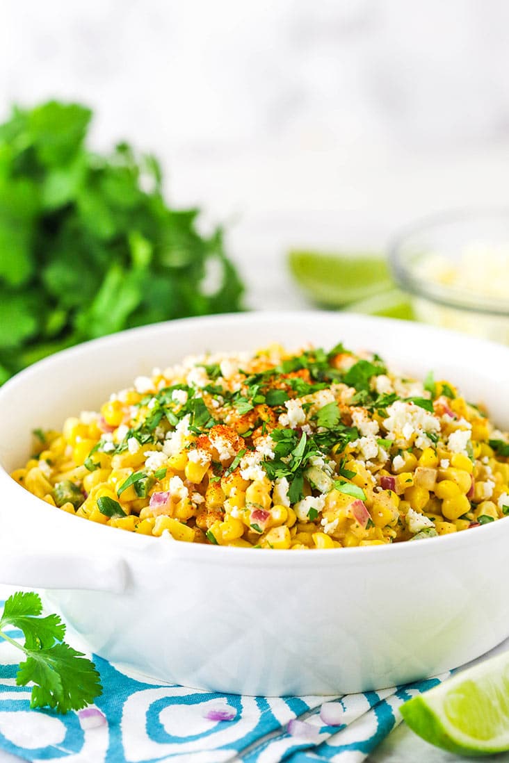 mexican street corn salad in white dish from the side with cilantro in the background