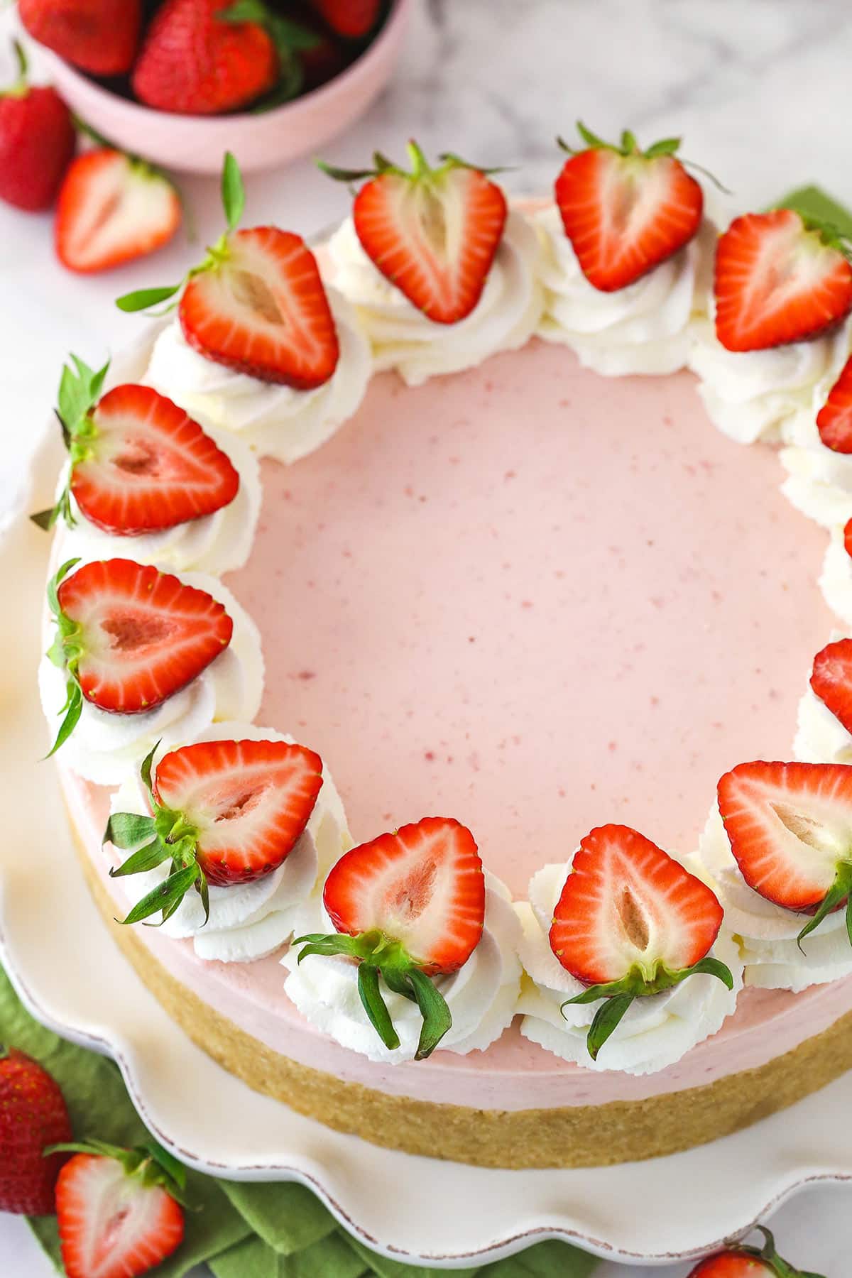 Overhead of a no back strawberry cheesecake on a serving platter near fresh strawberries.