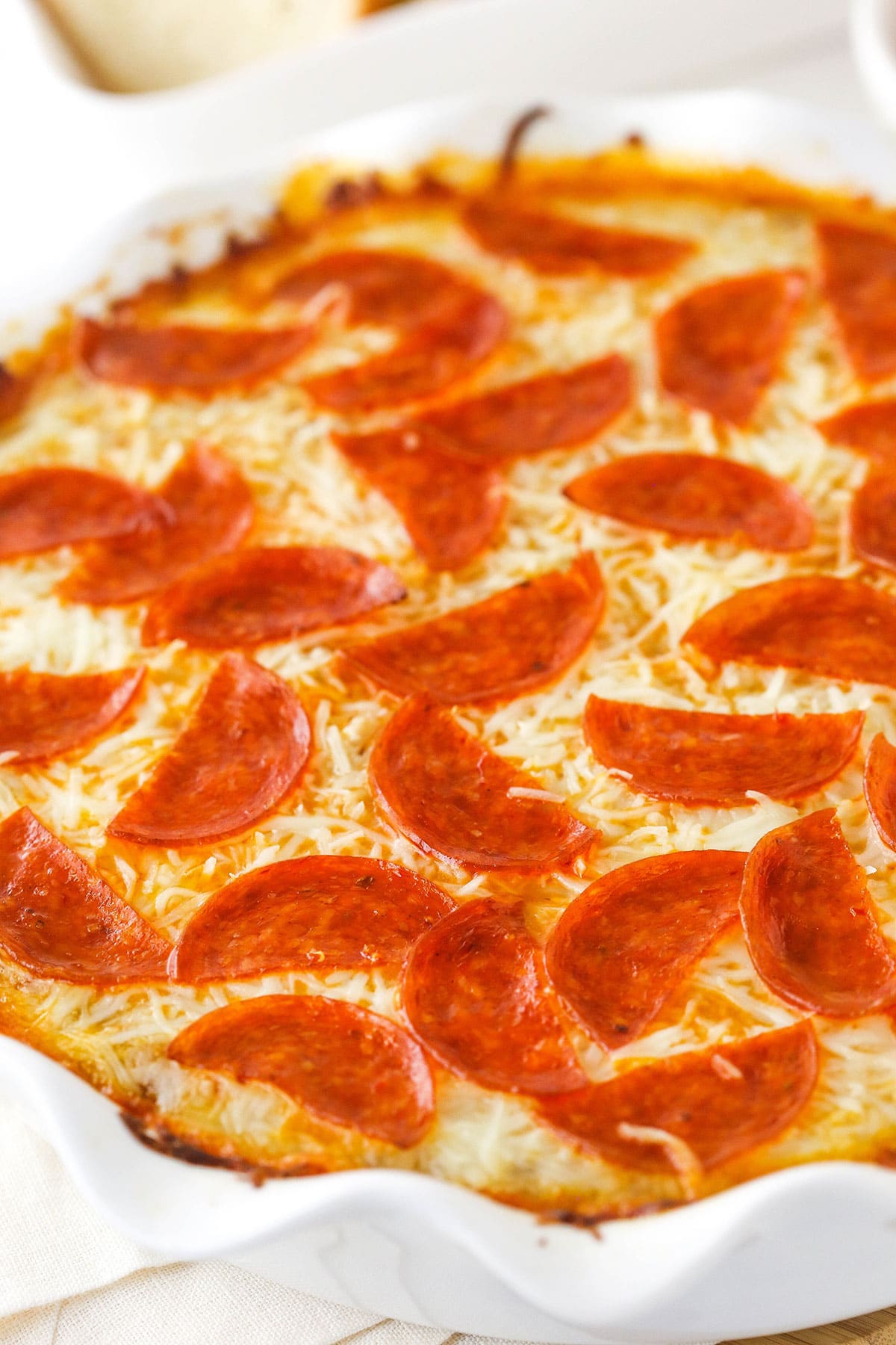 A fluted white pie pan, filled with hot pepperoni pizza dip.
