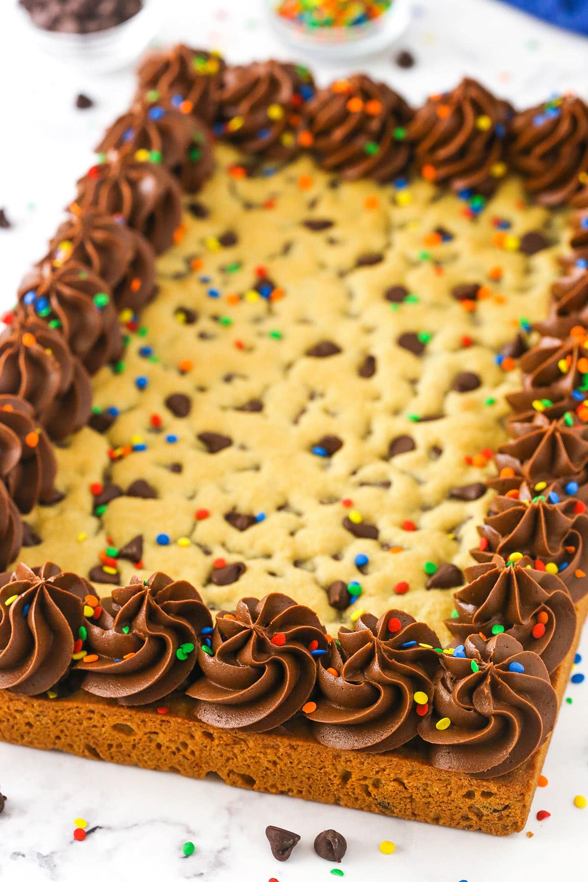 A chocolate chip cookie cake topped with swirls of chocolate frosting around the perimeter