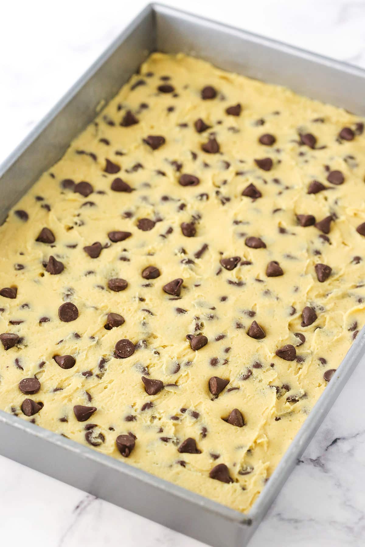 Chocolate chip cookie dough spread into a silver sheet pan