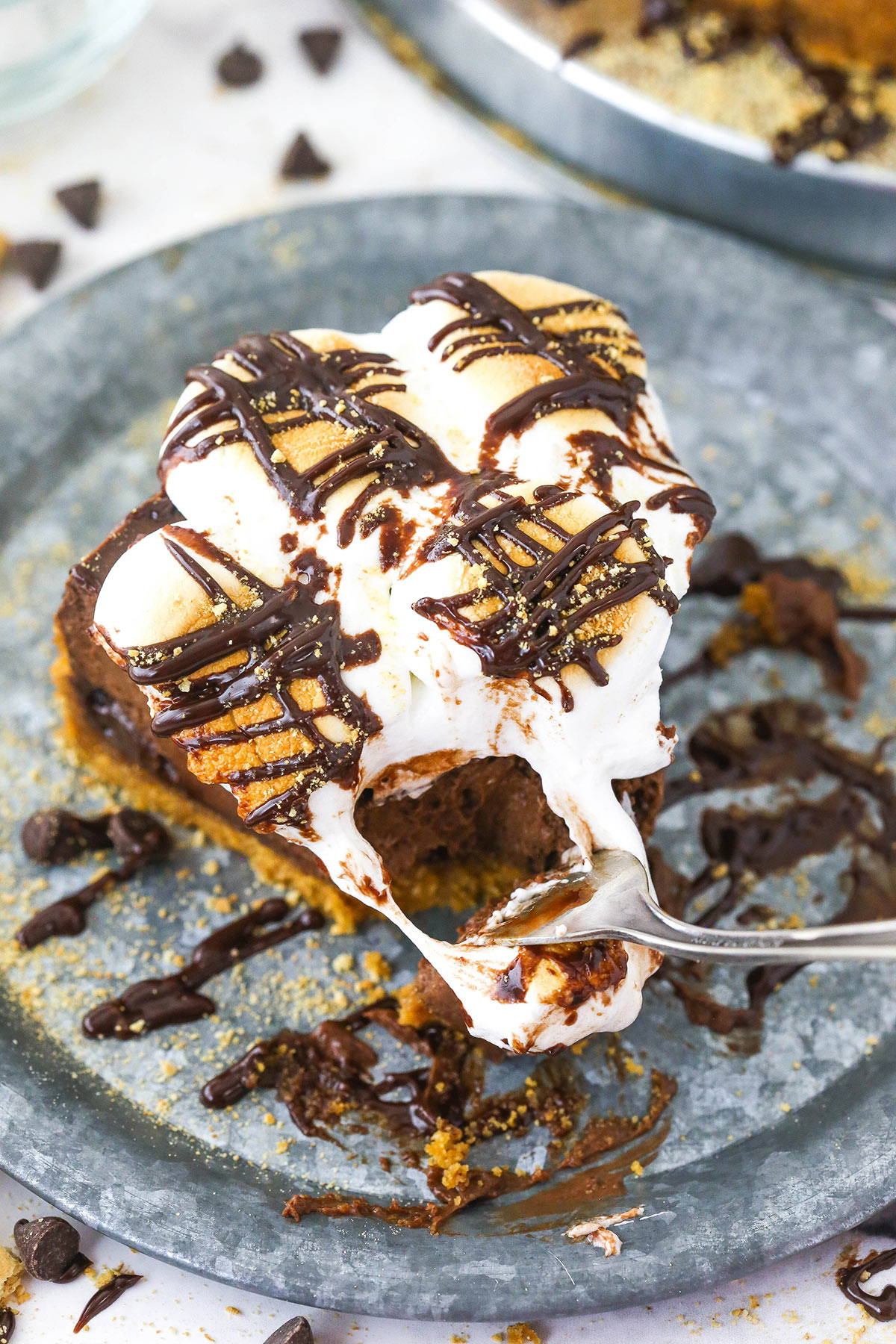 A fork digging into a slice of smores cheesecake with a warm, gooey marshmallow topping