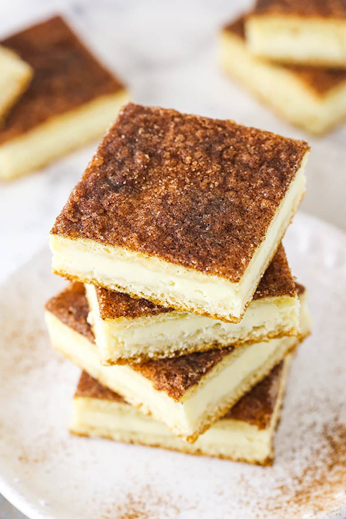 Four Cinnamon Sugar Cheesecake Bars Stacked on a White Plate