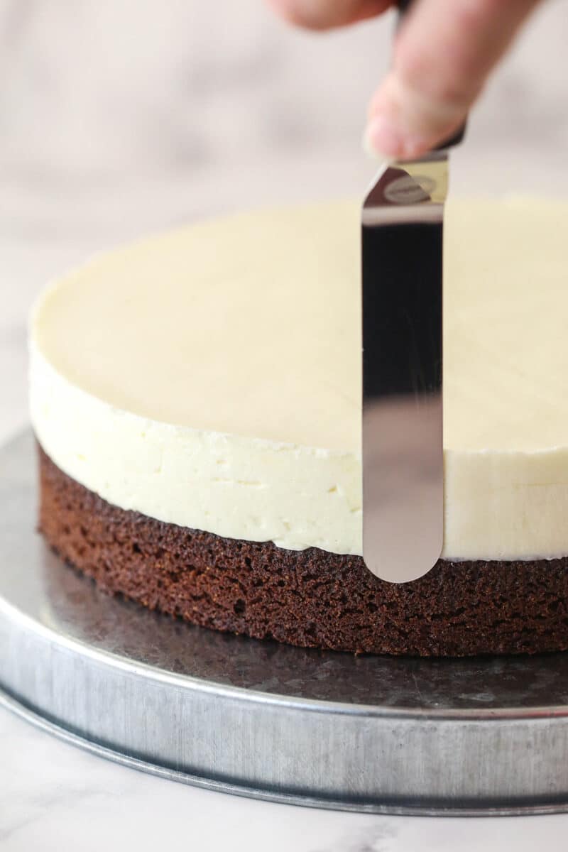 Smoothing out chilled no-bake cheesecake filling on top of a brownie base.