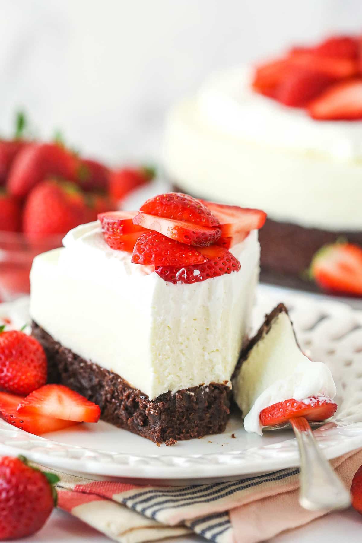 A slice of strawberry brownie cheesecake on a plate with a bite taken out of it.