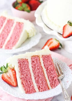 A Piece of Strawberry Cake on a Plate with a Sliced Strawberry Beside It
