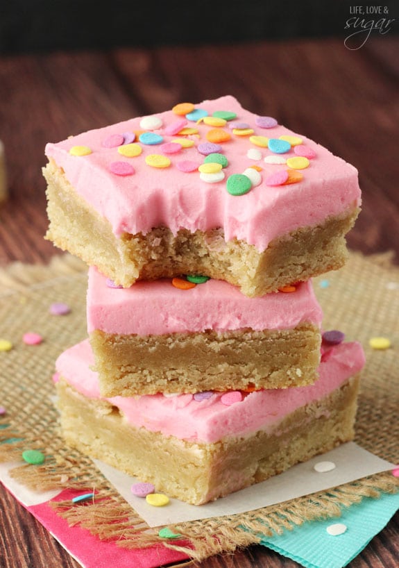 Pink Frosted Sugar Cookie Bars in a stack with a bite out of the top one